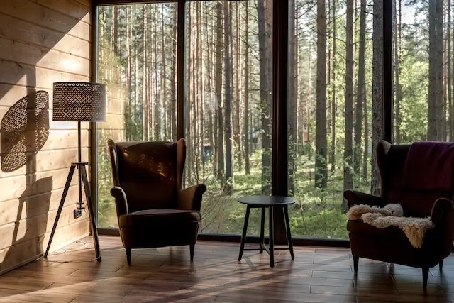 2 مبل تکی در اتاقی چوبی که پشت مبل ها سرتاسر شیشه وجود دارد ، منظره ی این اتاق جنگل است و فضای آرامش بخشی را ایجاد کرده